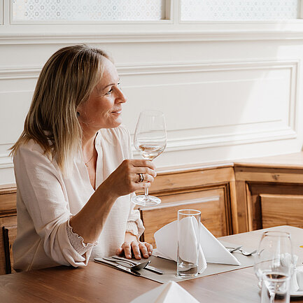 Dame mit einem Glas Weißwein im Restaurant Weitblick im Hotel das Eisenberg.
