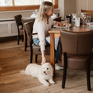Dame streichelt den Hund, der neben ihr beim Essen im Hotel das Eisenberg liegt.