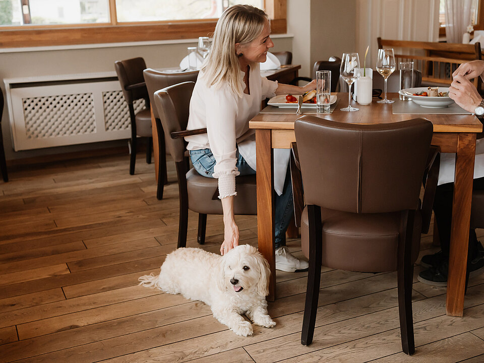 Dame streichelt den Hund, der neben ihr beim Essen im Hotel das Eisenberg liegt.