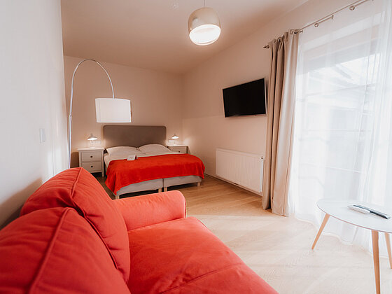Sitzecke mit Couch und Tisch mit Blick auf das Doppelbett im Landhaus Doppelzimmer Lavendel im Hotel das Eisenberg.