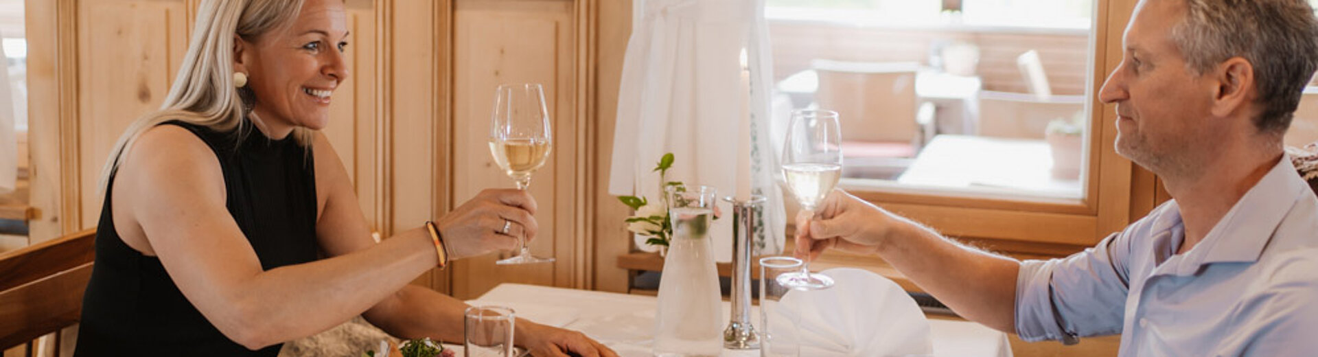 Dame und Herr sitzen am Tisch und stoßen an im Hotel das Eisenberg.
