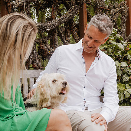 Dame und Herr sitzen mit Hund in der Gartenanlage vom Hotel das Eisenberg.